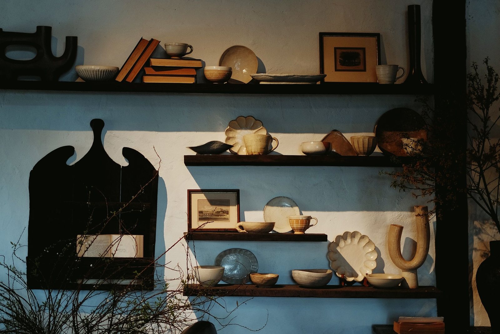 Koyu raflarda seramikler, kitaplar ve küçük sanat objelerinden oluşan sıcak ev seçkisi